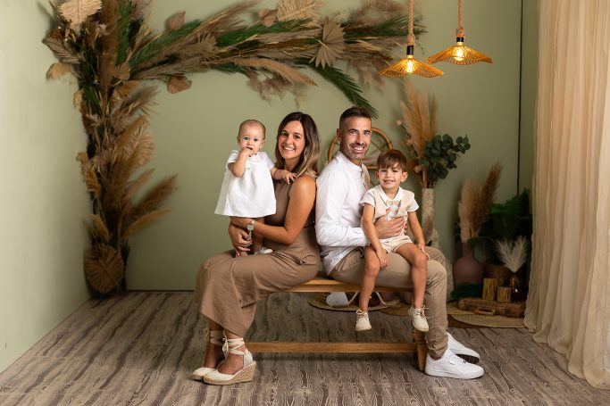 Familia sonriente posando juntos en un entorno decorado con plantas y muebles de madera.