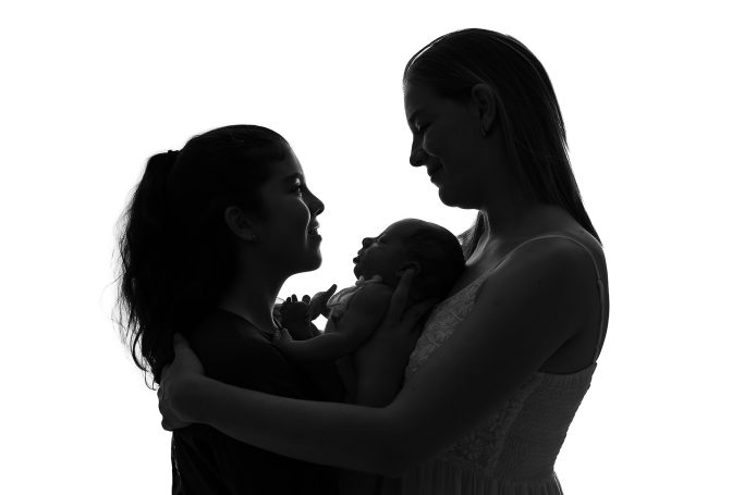 Siluetas de dos mujeres sosteniendo un bebé entre ellas, mostrando ternura y amor.