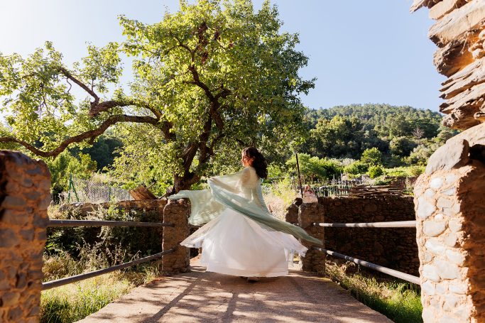 Mujer con vestido blanco girando en un entorno natural con árboles y montañas.